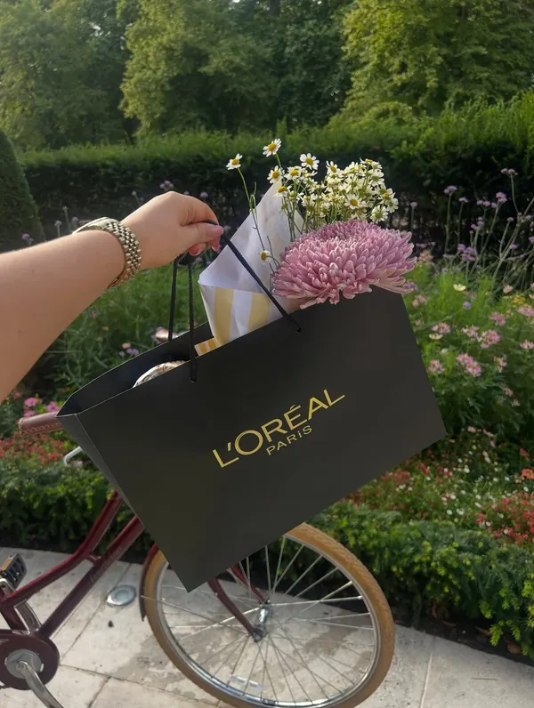 A L’Oréal gift bag and a bouquet of flowers held outdoors against a leafy garden.